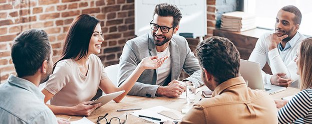 Group of young business people discussing something while sitting at the wooden table together