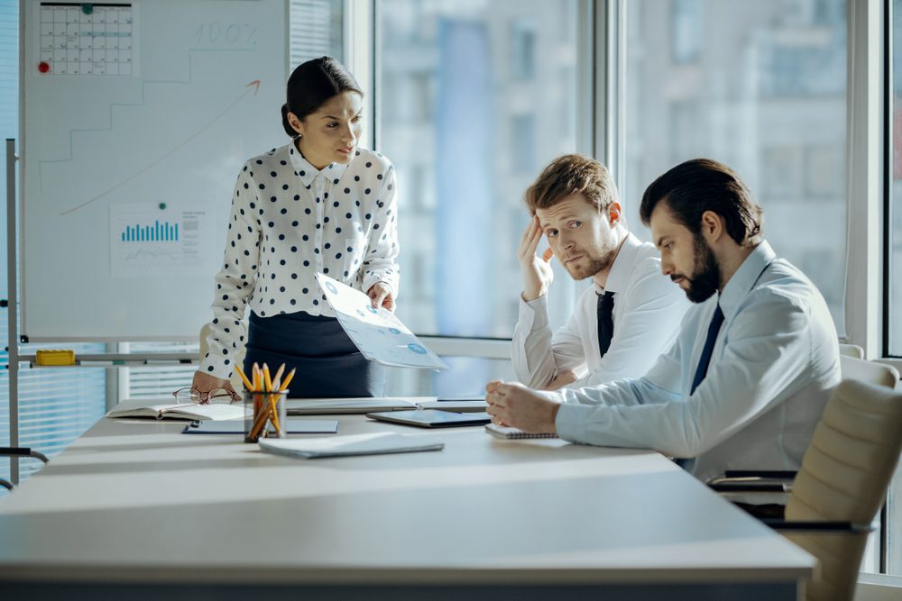 Angry female boss having a meeting with her employees and reprimanding them for the poor performance while they looking embarrassed